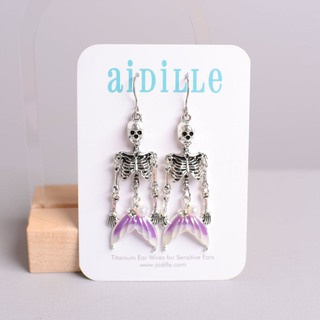 Skeleton-themed earrings on a 'aidille' branded card with a light gray background