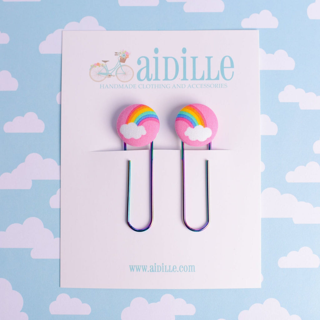 Paper clips with rainbow designs on a card with 'aidille' branding against a cloud-patterned background.