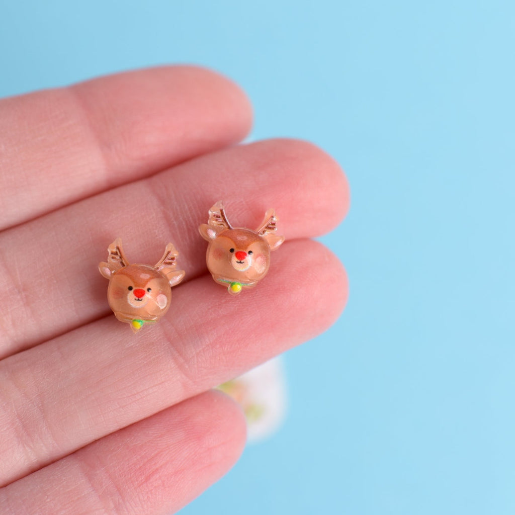 Deer-shaped earrings held between fingers against a light blue background