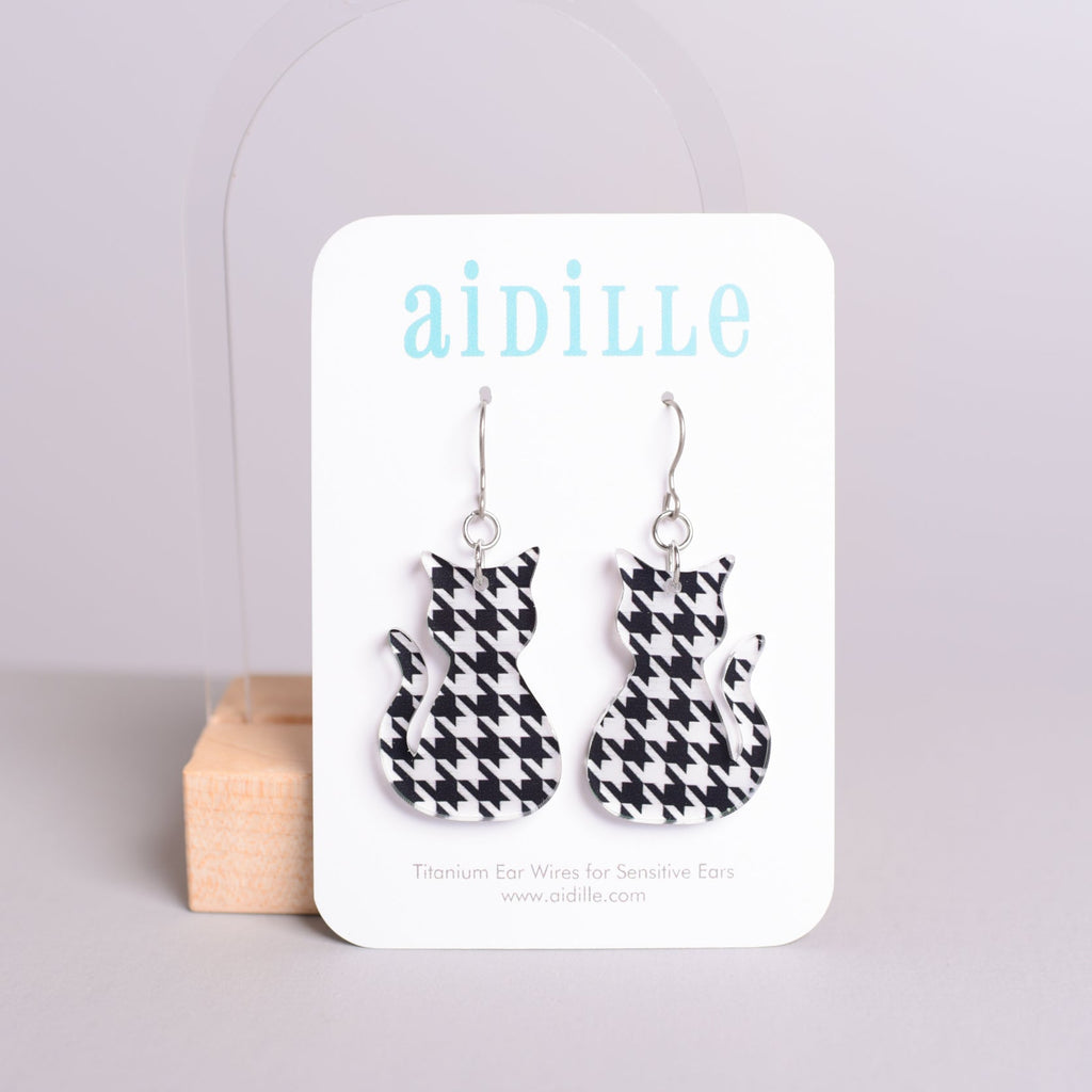 Houndstooth pattern cat-shaped earrings on a 'aidille' branded card against a light gray background