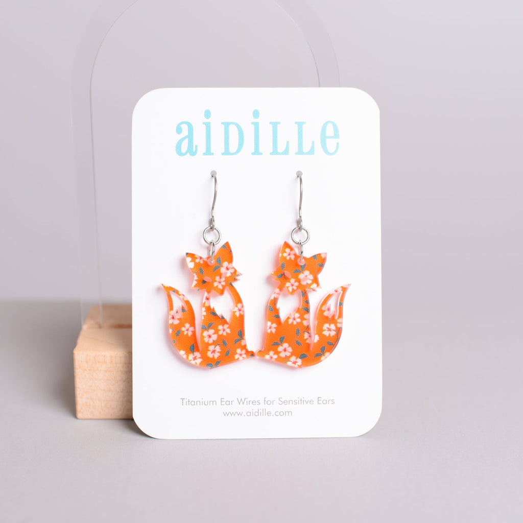 Orange fox earrings on a 'aidille' branded card against a light gray background