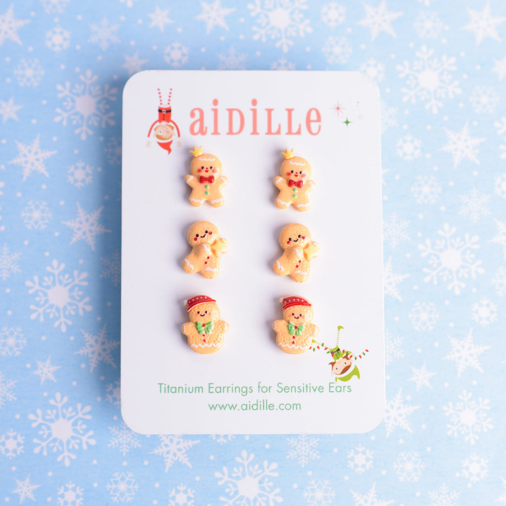 Set of gingerbread-themed earrings on a card with 'aidille' branding against a snowflake patterned background.