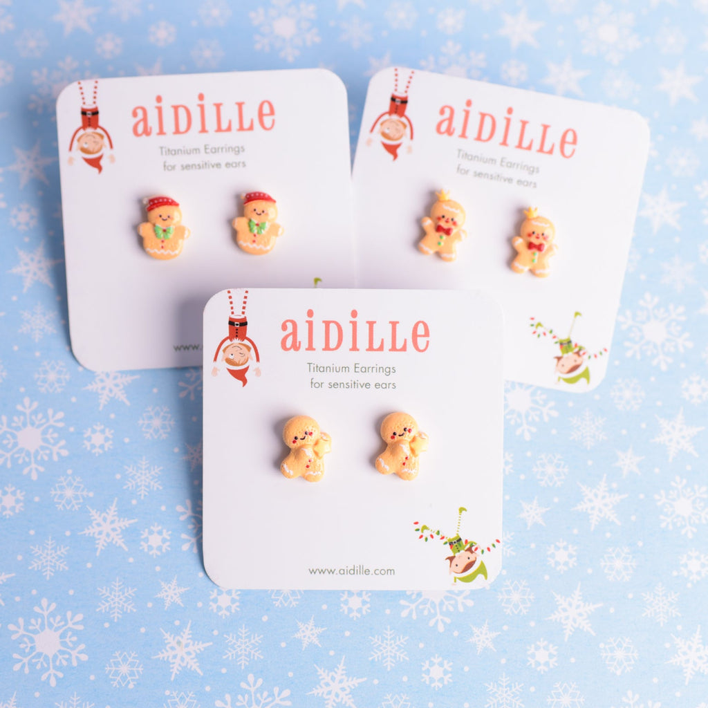 Three pairs of earrings on 'aidille' branded cards against a blue background with snowflake patterns.
