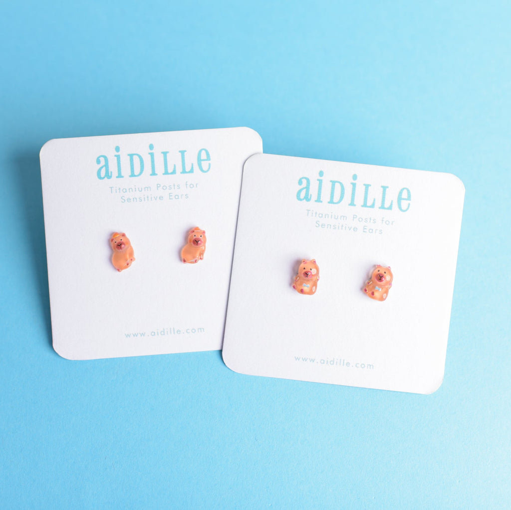 Pair of small earrings on 'aidille' branded cards against a blue background