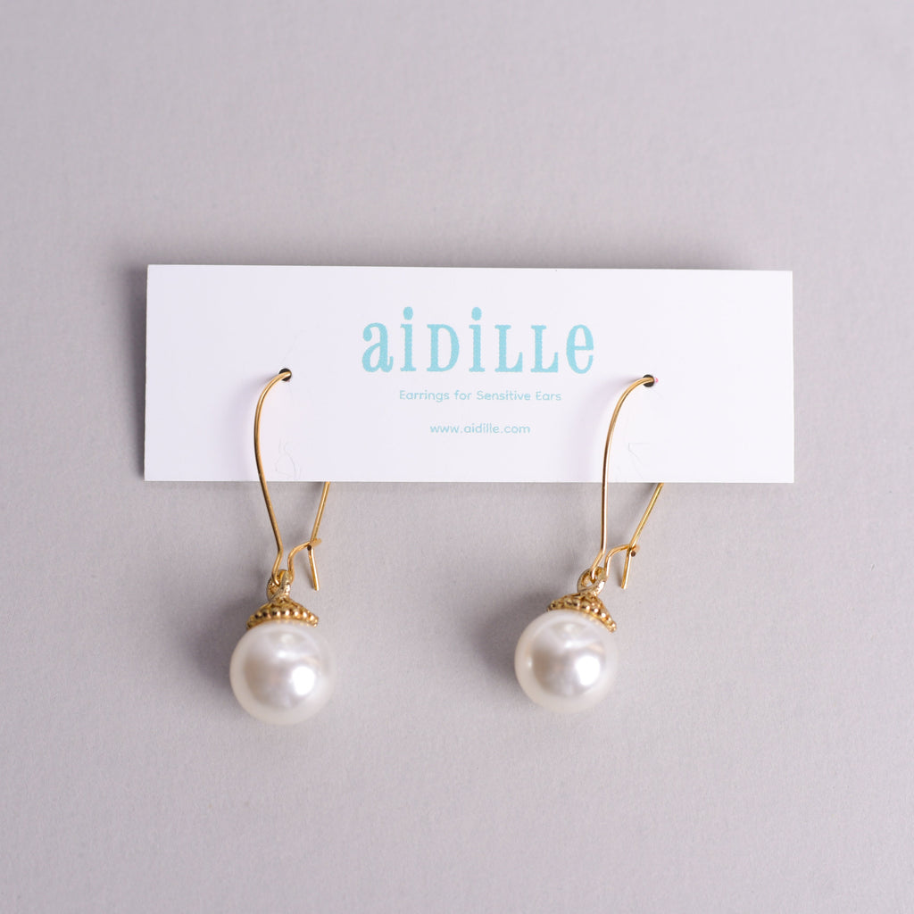 Pearl earrings with gold hooks on a 'aidille' branded card against a gray background