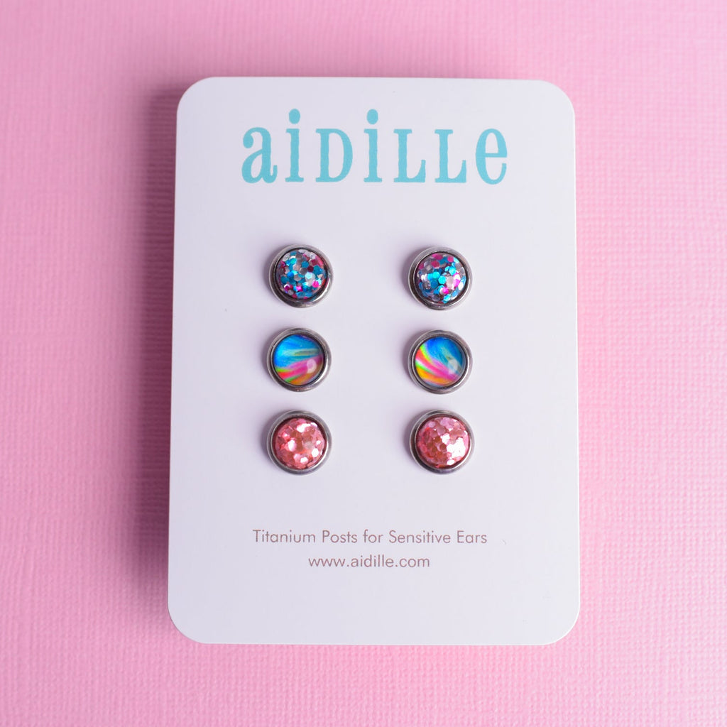 Set of colorful earrings on a 'aidille' branded card against a pink background