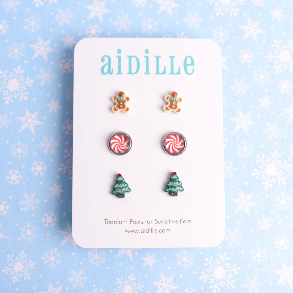 Set of Christmas-themed earrings on a 'aidille' branded card with a snowflake patterned background.