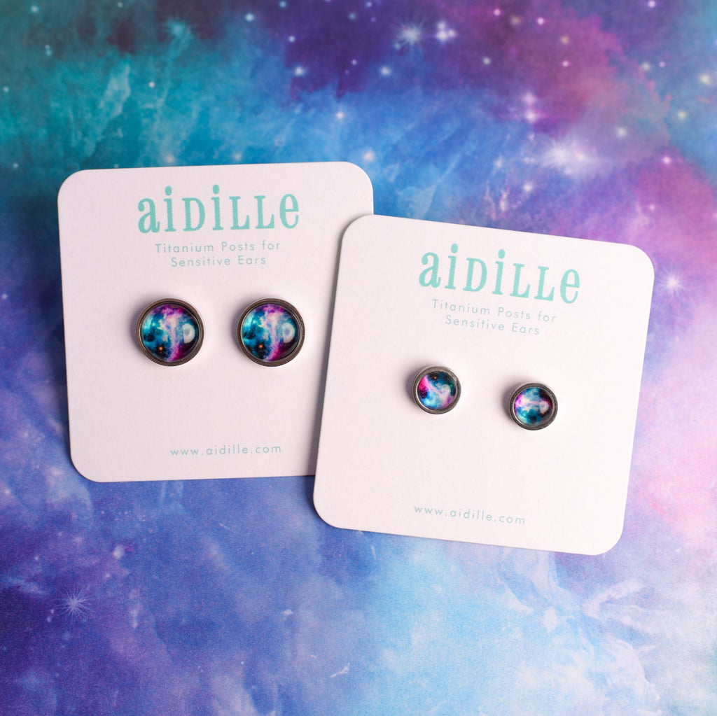 Pair of earrings on 'aidille' branded cards against a colorful cosmic background